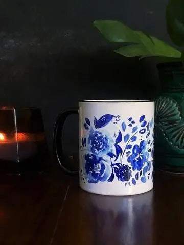 White ceramic blue floral mug with black handle and rim on wooden table