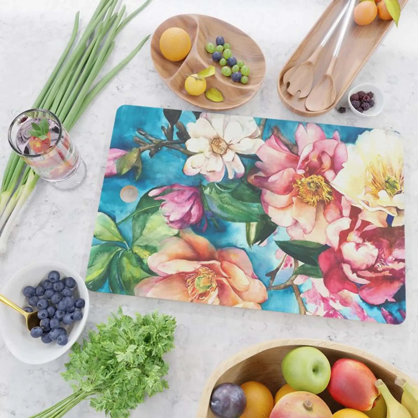 Tropical Floral I Glass Cutting Board with vibrant watercolor flowers on a kitchen countertop surrounded by fresh fruits and herbs